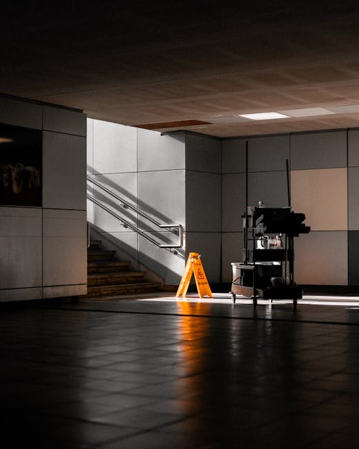 An indoor commercial space with a tiled dark floor and a grey tiled wall. A set of stairs with metal handrails leads upwards, illuminated by natural light entering from an unseen source. The floor app